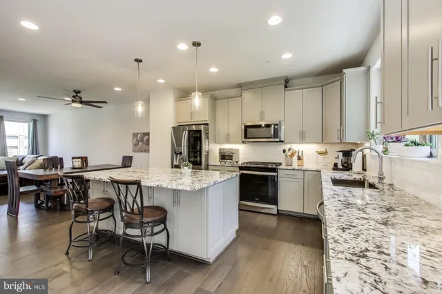 a kitchen with stainless steel appliances kitchen island granite countertop a table chairs sink and cabinets
