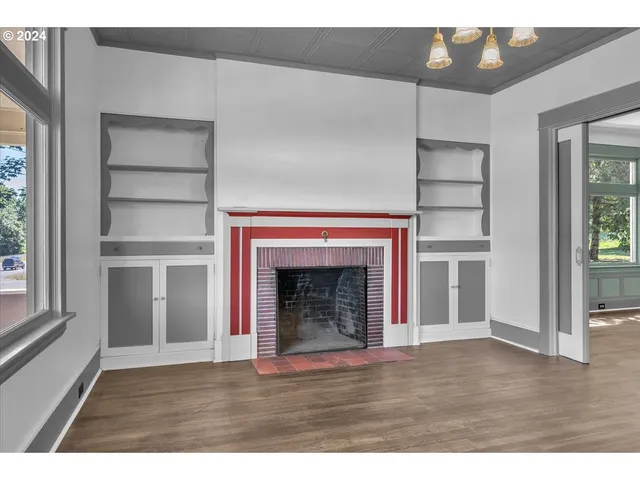 a view of an empty room with wooden floor fireplace and a window