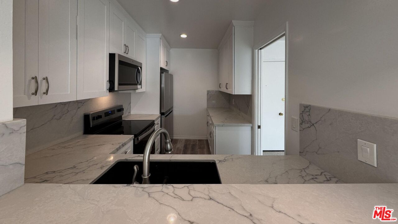 11750 Sunset Boulevard, Unit 317 Los Angeles, CA 90049 - Photo 3 of 11 a kitchen with granite countertop a refrigerator a microwave a sink and cabinets