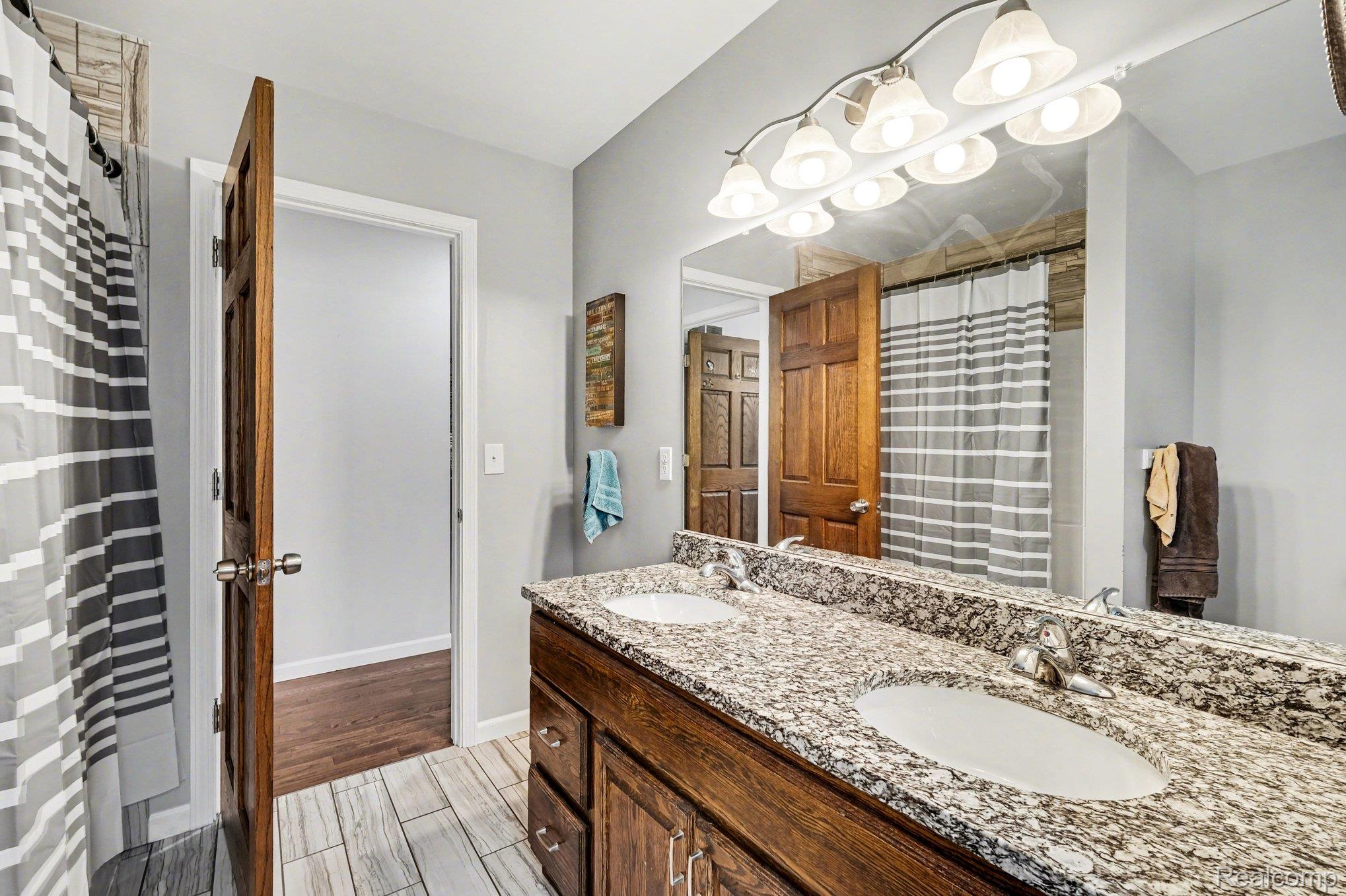 2800 Meadowdale Road Metamora, MI 48455 - Photo 16 of 28 Bathroom featuring double vanity, wood finish floors, and a shower with shower curtain