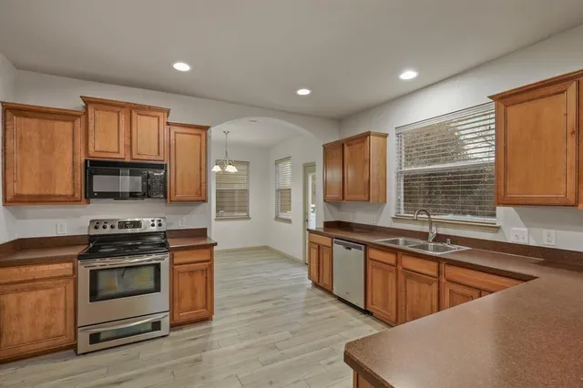 a kitchen with stainless steel appliances granite countertop wooden cabinets a sink a stove a microwave and wooden floors