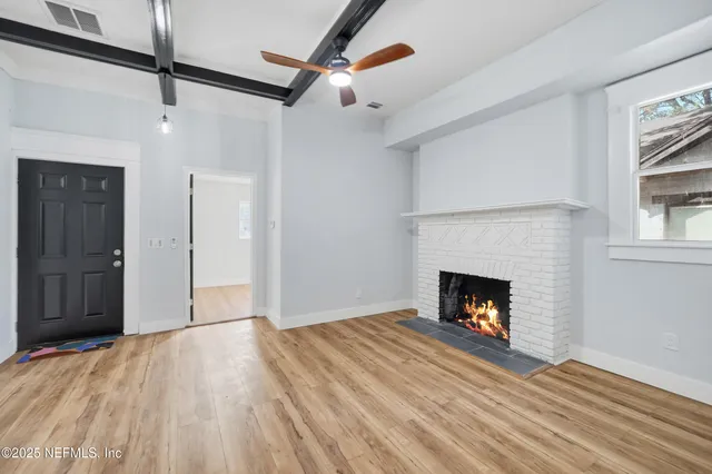a view of an empty room with wooden floor fireplace and a window