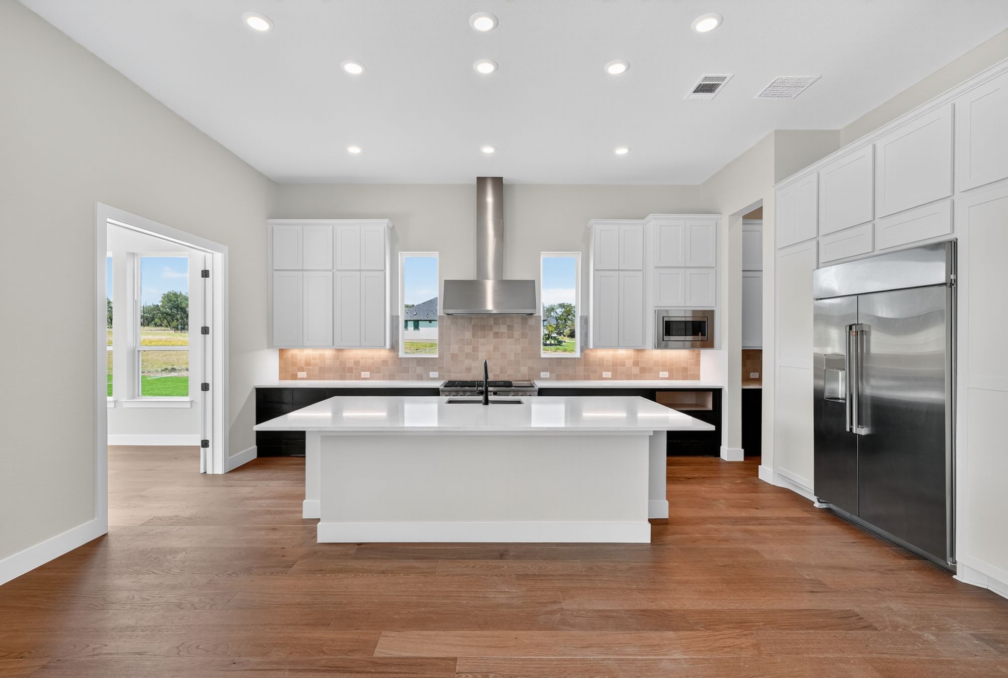 205 Three Rivers Road Georgetown, TX 78633 - Photo 7 of 32 Kitchen featuring tasteful backsplash, white cabinetry, built in appliances, an island with sink, and light wood-style flooring