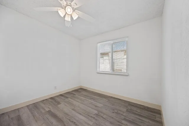 an empty room with wooden floor chandelier fan and window