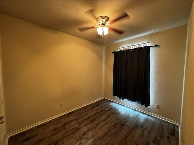 an empty room with a chandelier fan and wooden floor