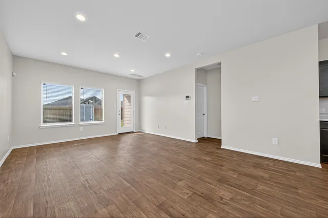 a view of an empty room with wooden floor and windows