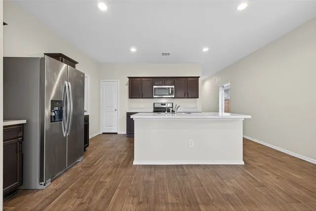 a view living room with stainless steel appliances a refrigerator a sink a stove a microwave and wooden floors