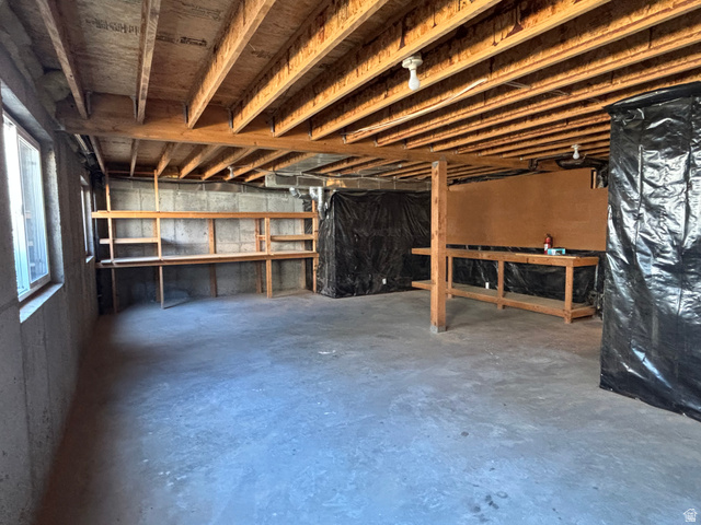 798 South 600 East Payson, UT 84651 - Photo 28 of 31 Unfinished basement featuring exposed wood beams, concrete foundation walls, two windows providing natural light, built-in shelving, and a large workbench