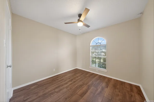 an empty room with wooden floor chandelier fan and windows
