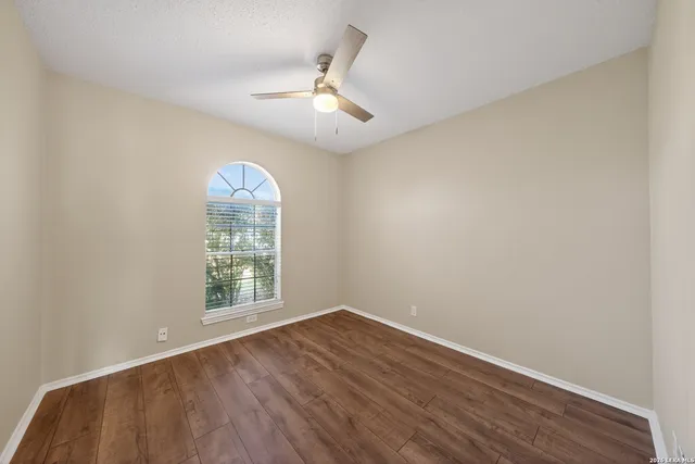 an empty room with wooden floor chandelier fan and windows