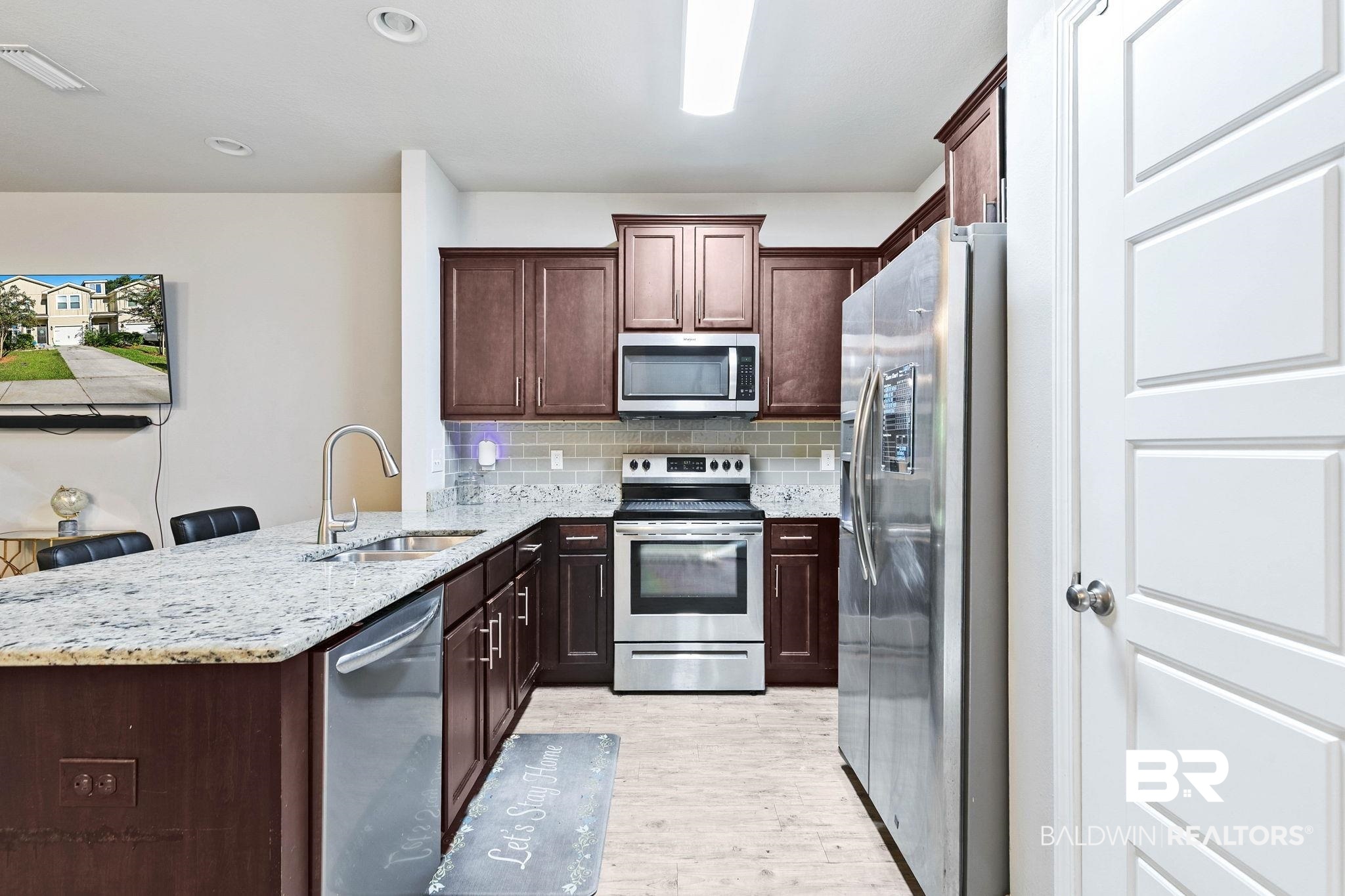 25806 Pollard Road, Unit 24 Daphne, AL 36526 - Photo 10 of 33 Kitchen featuring decorative backsplash, appliances with stainless steel finishes, light stone counters, a peninsula, and dark brown cabinets