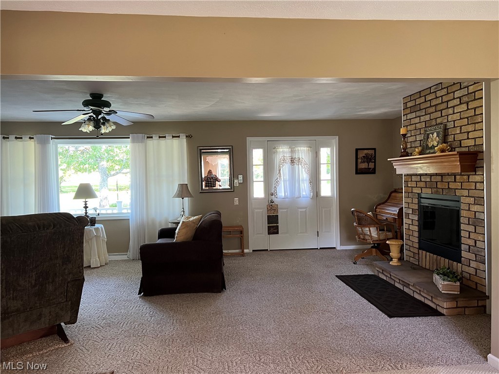 3191 Ninety Road Ashtabula, OH 44004 - Photo 9 of 22 Carpeted living room with a fireplace, brick wall, and ceiling fan