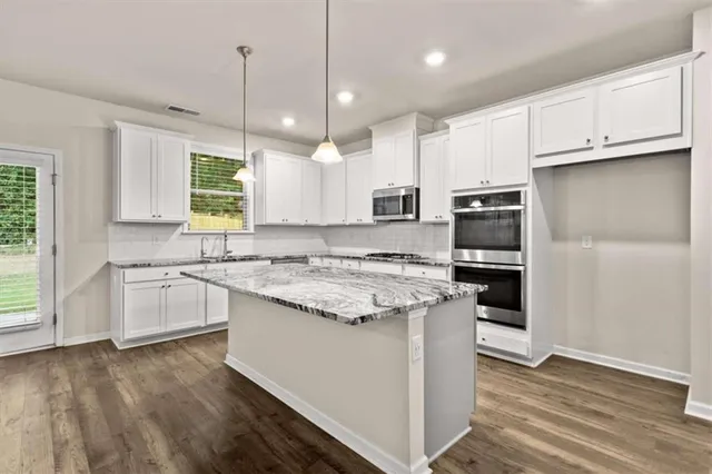 a kitchen with kitchen island granite countertop a stove a sink and white cabinets with wooden floor