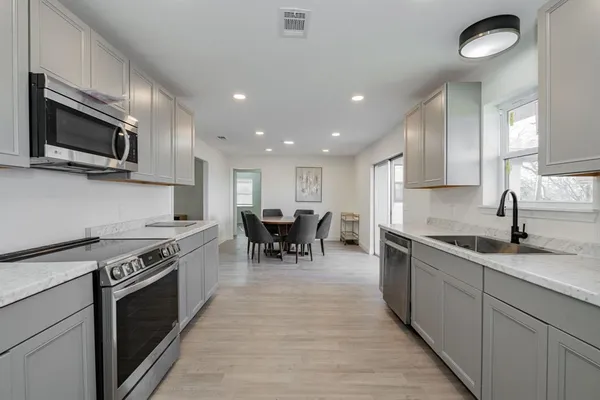 a kitchen with stainless steel appliances granite countertop a stove top oven a sink dishwasher a dining table and chairs with wooden floor