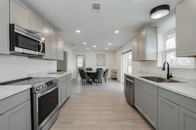 a kitchen with stainless steel appliances granite countertop a stove top oven a sink dishwasher a dining table and chairs with wooden floor