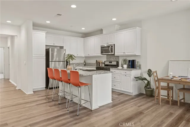 a kitchen with stainless steel appliances kitchen island granite countertop a stove top oven a sink a refrigerator and white cabinets