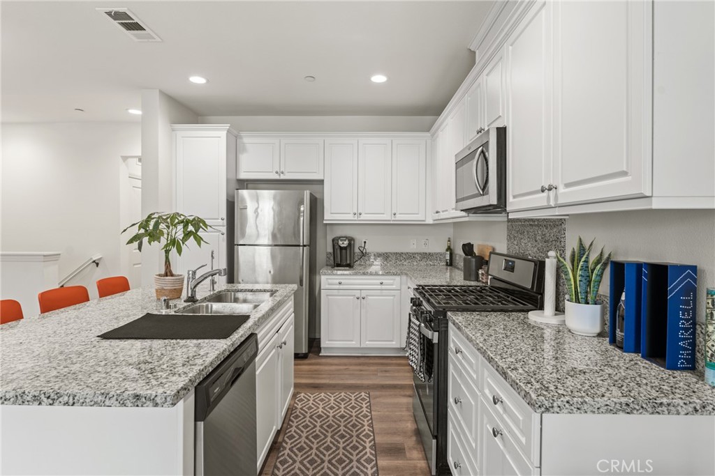 2845 East Berry Loop Privado, Unit 33 Ontario, CA 91761 - Photo 9 of 17 a kitchen with kitchen island granite countertop a sink stainless steel appliances and white cabinets