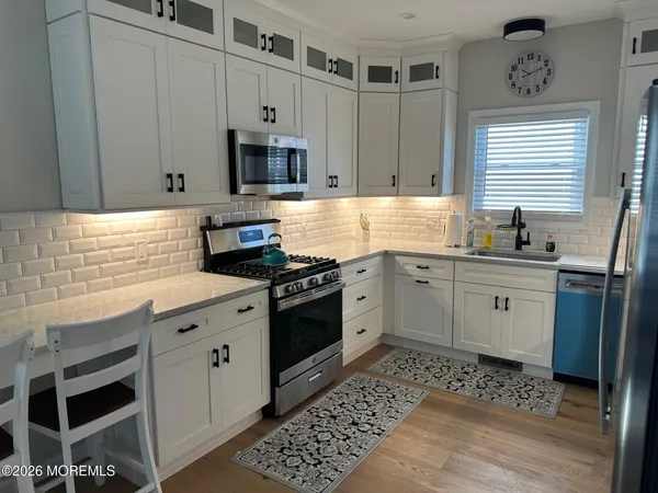 a kitchen with stainless steel appliances white cabinets a sink a stove a microwave and wooden floors