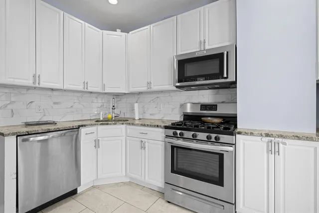 a kitchen with stainless steel appliances granite countertop grey cabinets a stove a sink and a microwave