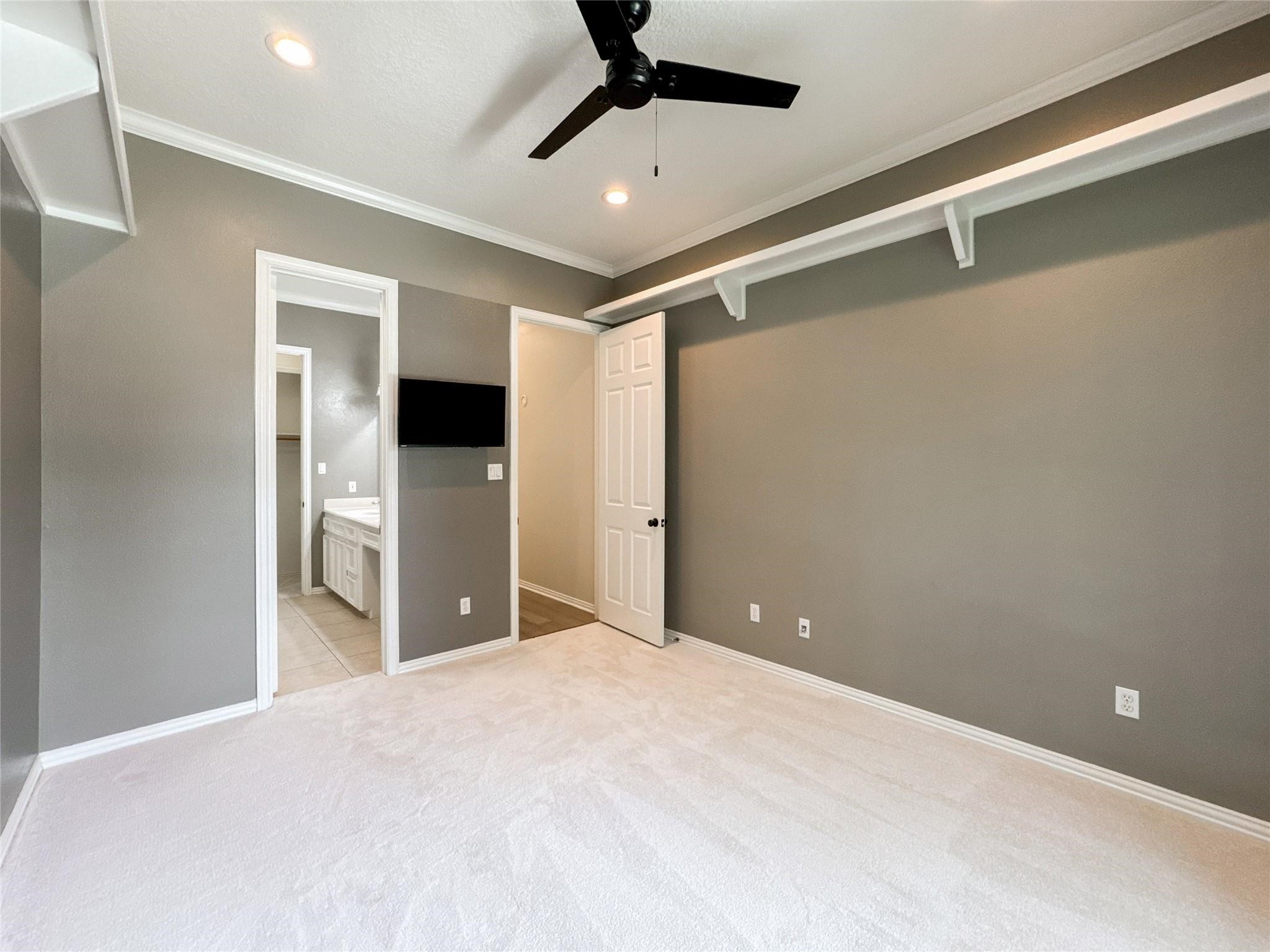1810 Woerner Road Houston, TX 77090 - Photo 28 of 39 This room features neutral gray walls, a white ceiling with recessed lighting, and a ceiling fan. It has an attached bathroom visible through a doorway, and light-colored carpeting. The space is simple and modern, offering a blank canvas for personalization.
