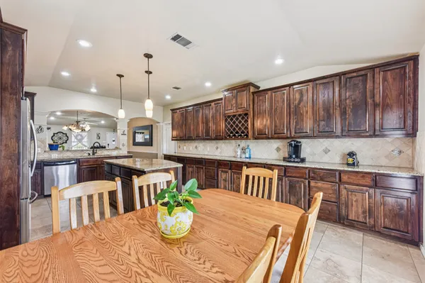 a kitchen with stainless steel appliances kitchen island granite countertop a dining table chairs and a white cabinets