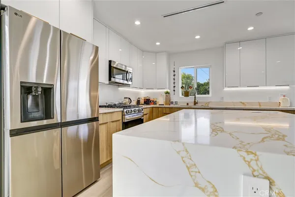 a kitchen with stainless steel appliances granite countertop a refrigerator a sink and a stove with wooden floor