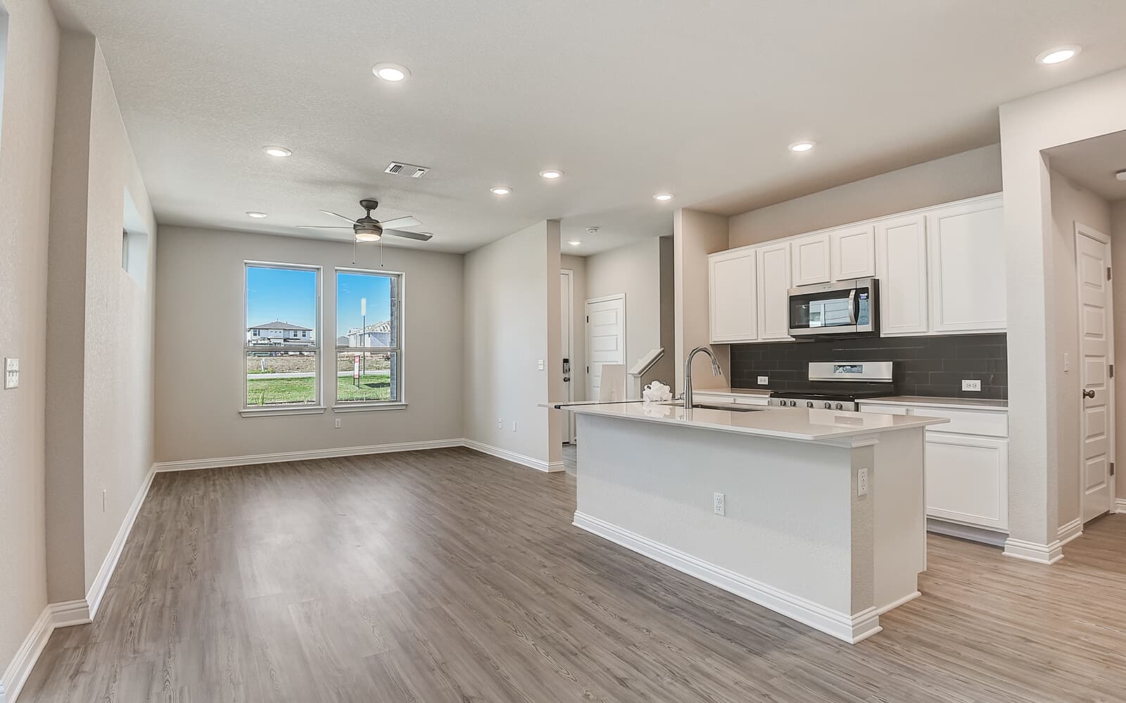 8209 Springsteen Drive Austin, TX 78744 - Photo 2 of 11 Kitchen with an island with sink, stainless steel appliances, white cabinetry, a ceiling fan, and tasteful backsplash
