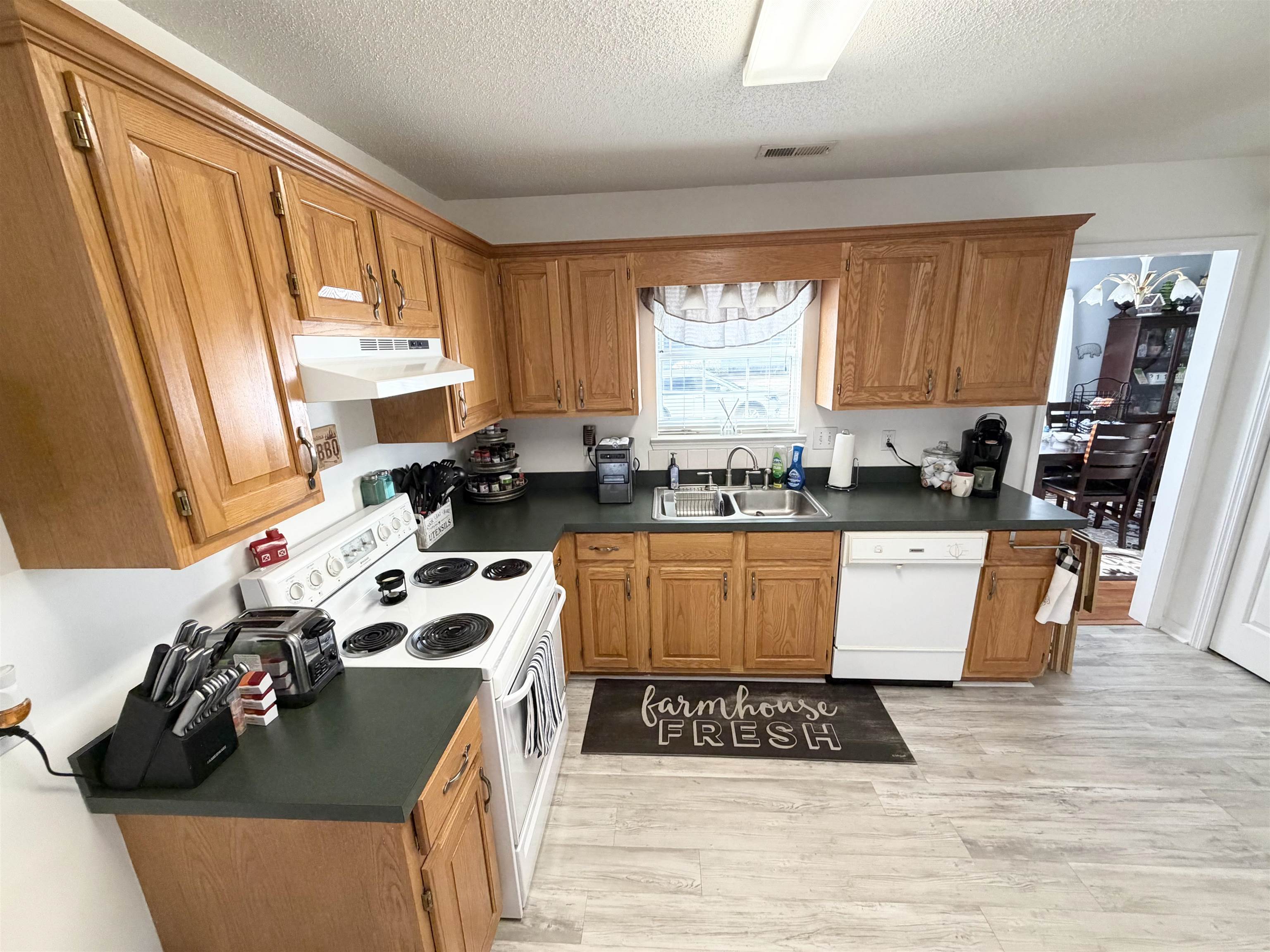 106 Sly Fox Trail Myrtle Beach, SC 29588 - Photo 6 of 14 Kitchen with dark countertops, white appliances, brown cabinets, under cabinet range hood, and a textured ceiling