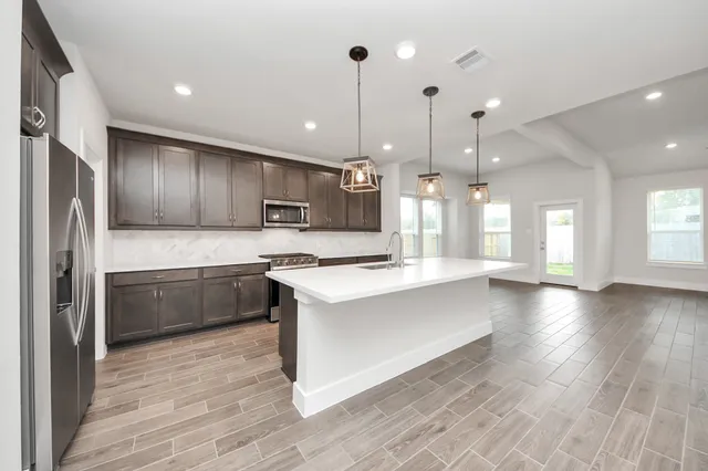 a large kitchen with granite countertop a large counter top a sink stainless steel appliances and cabinets