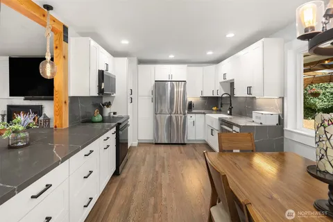 a kitchen with stainless steel appliances a refrigerator a sink dishwasher a stove top oven a dining table and chairs with wooden floor