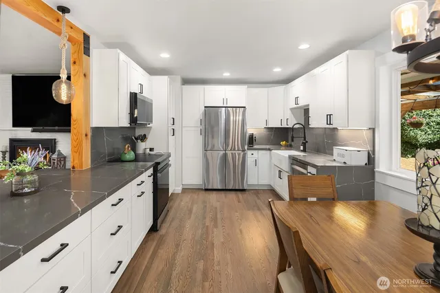 a kitchen with stainless steel appliances a refrigerator a sink dishwasher a stove top oven a dining table and chairs with wooden floor