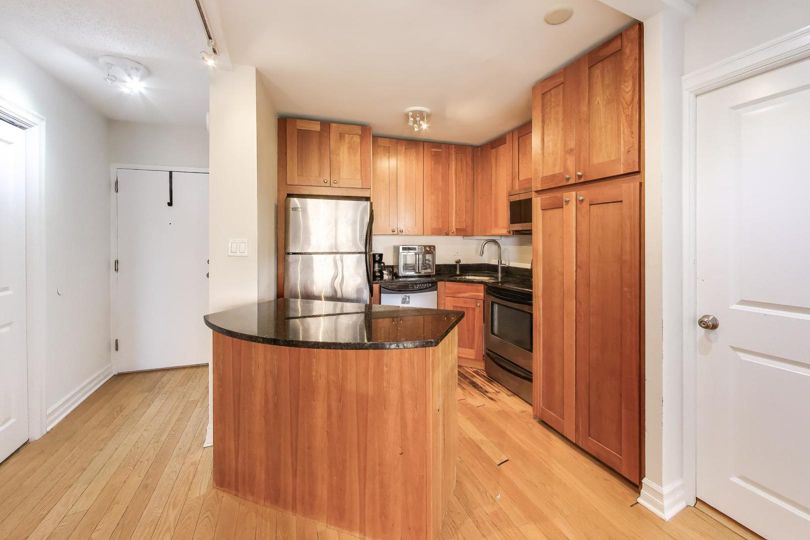 2930 North Sheridan Road, Unit 702 Chicago, IL 60657 - Photo 7 of 25 a kitchen with kitchen island granite countertop wooden floors and stainless steel appliances