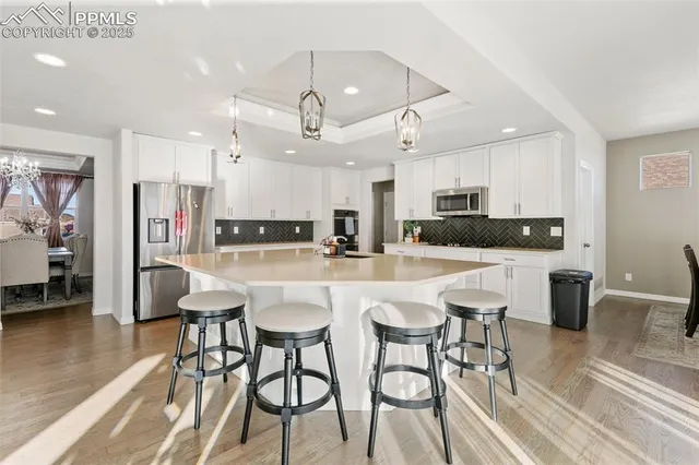 a kitchen with stainless steel appliances kitchen island granite countertop a dining table chairs and a refrigerator