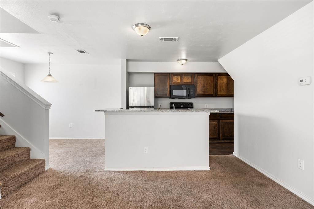 9837 Walnut Street, Unit S203 Dallas, TX 75243 - Photo 6 of 26 Open concept living area with carpeting, a kitchen featuring dark wood cabinetry, a stainless steel refrigerator, and a black microwave