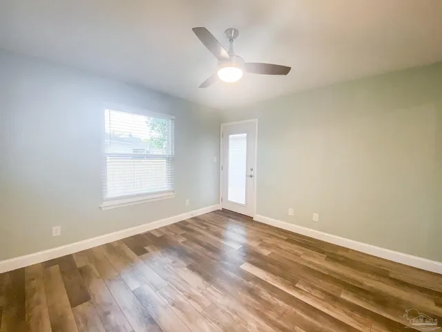 an empty room with wooden floor ceiling fan and windows