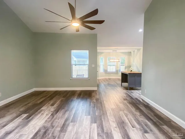 an empty room with wooden floor fan and windows
