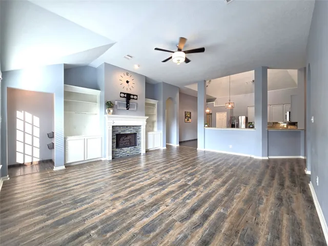a view of a livingroom with a fireplace a ceiling fan and wooden floor