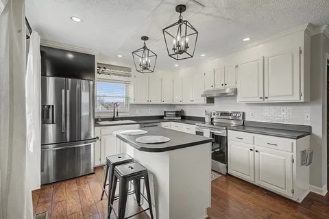 a kitchen with stainless steel appliances granite countertop a sink a stove a refrigerator and island with wooden floor