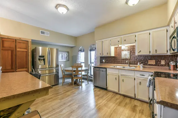 a kitchen with stainless steel appliances granite countertop a refrigerator a stove a sink dishwasher and white cabinets with wooden floor