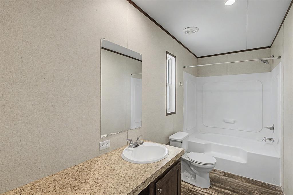 177 New Highland Road Springtown, TX 76082 - Photo 22 of 40 Bathroom featuring a white integrated tub and shower unit, wood-finish flooring, a vanity with a light-toned countertop, and a rectangular mirror