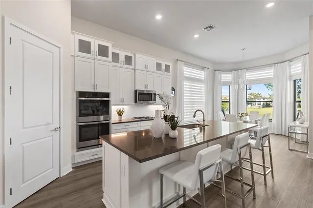 a kitchen with stainless steel appliances granite countertop a stove a sink a refrigerator white cabinets and wooden floor