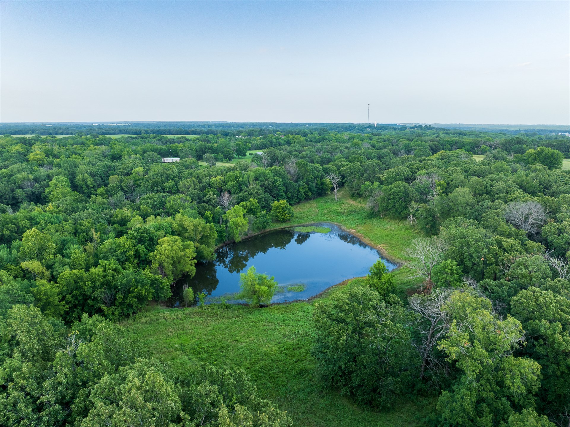 15291 East 400 Road Claremore, OK 74017 - Photo 67 of 96 Expansive natural setting featuring a reflective pond, dense mature trees, and open grassy areas