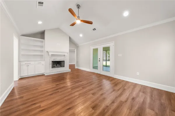 a view of an empty room with wooden floor and a kitchen