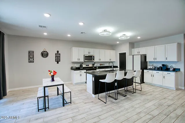 a kitchen with stainless steel appliances granite countertop a refrigerator a stove top oven and a dining table with wooden floor