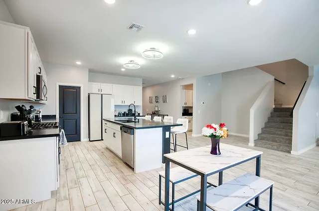 a kitchen with stainless steel appliances kitchen island granite countertop a table chairs stove and white cabinets