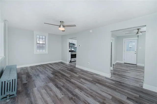 an empty room with wooden floor chandelier fan and windows