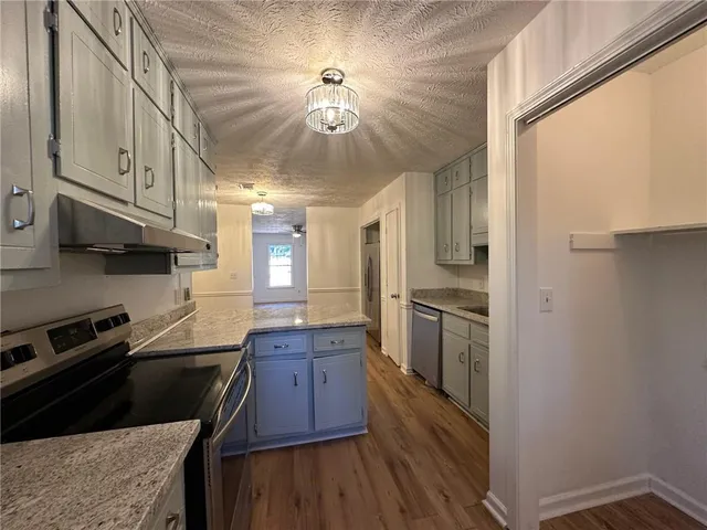 a kitchen with stainless steel appliances granite countertop a refrigerator a sink dishwasher a stove and white countertops with wooden floor