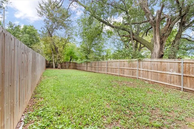 a view of a backyard with wooden fence and large trees