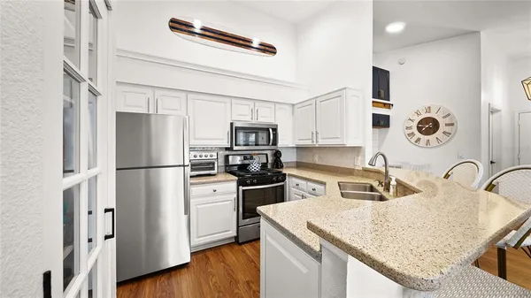 a kitchen with stainless steel appliances granite countertop a refrigerator a stove a sink and white cabinets with wooden floor