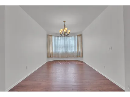 a view of an empty room with chandelier and wooden floor